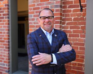 Financial advisor in professional attire poses confidently against brick backdrop, ready to assist with wealth management.