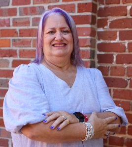 Financial advisor with purple-tinted hair smiling confidently in professional headshot for wealth management consultation.