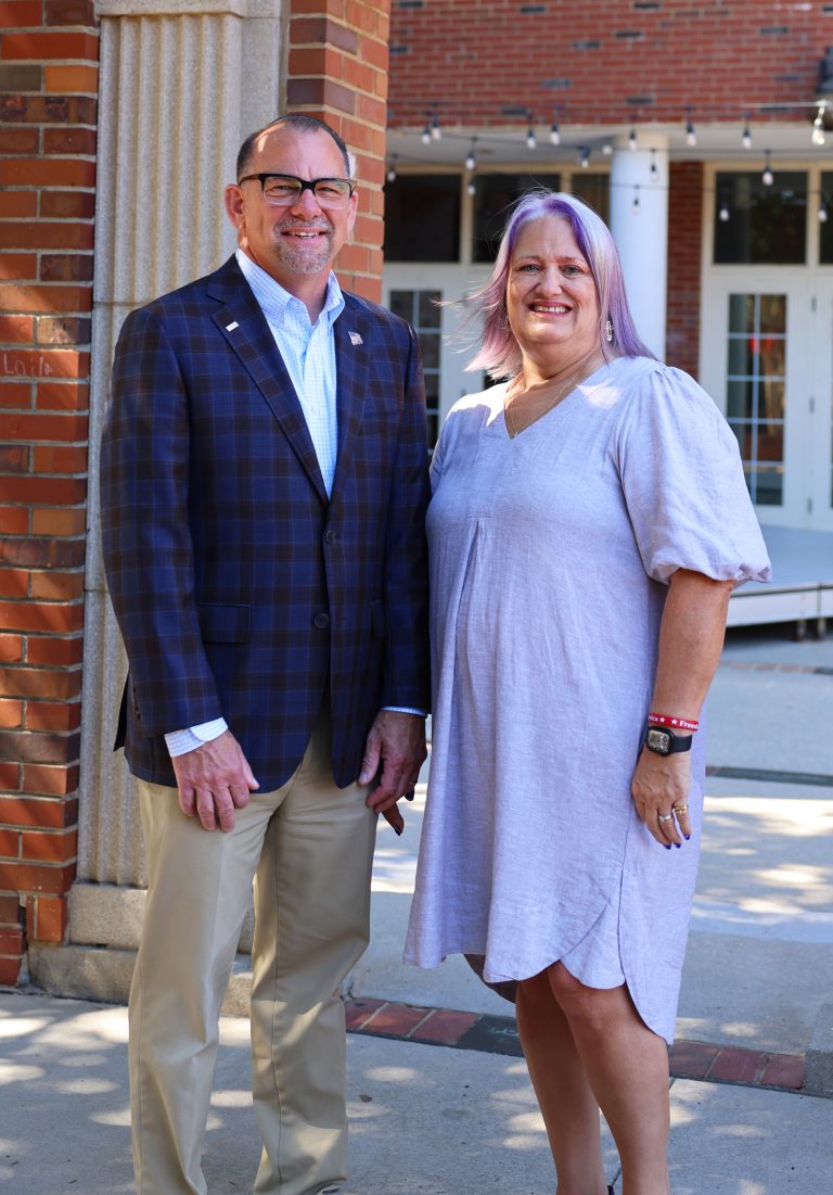 Two financial advisors smile together outside a modern brick building, representing Freitas Wealth Management's team in.